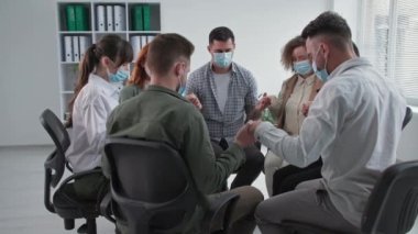 Bir grup genç, tıbbi maskeli, yüreği Tanrı 'ya inanan, el ele tutuşan ve terapi sırasında daire şeklinde bir koltukta otururken dua eden bir grup genç.