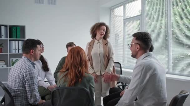 Thérapie de groupe, jeune groupe d'hommes et de femmes parlent de leurs problèmes pendant la session avec psychologue assis sur des chaises en cercle — Video