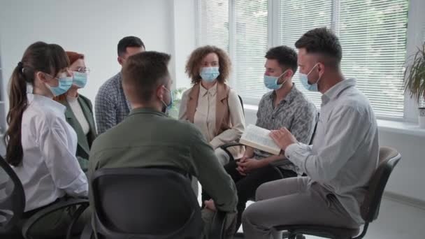 Evangelisation, junge Männer und Frauen in medizinischen Masken bei der Gruppentherapie Bibel lesen mit Glauben und Hoffnung auf Gott sitzen auf Stühlen im Kreis — Stockvideo