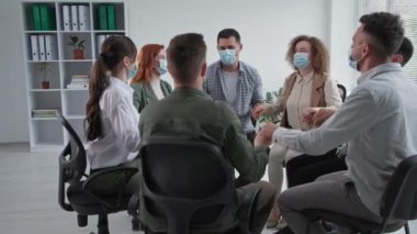 Grup desteği, tıbbi maske takan genç erkek ve kadınlar motivasyon eğitimi sırasında el ele tutuşup birbirlerini alkışlıyorlar.
