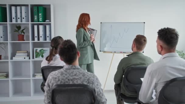 Confident female speaker-coach makes corporate presentation on flipchart teaching staff in group meeting during business meeting, young man raises his hand and asks question during presentation — 비디오