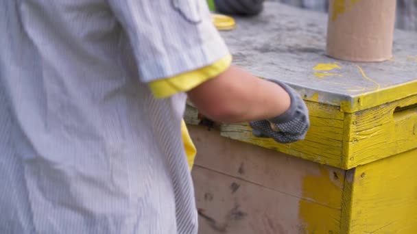 Літній чоловічий пасічник і маленький хлопчик фарбують дерев'яні вулики в теплий день на пасіці — стокове відео