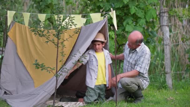 Dětství, starostlivý dědeček se baví se svým vnukem při venkovní rekreaci, hrát ve wigwam pozadí zelených stromů v zahradě — Stock video