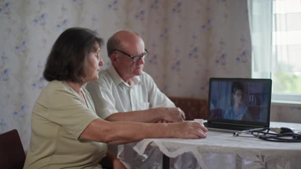 Opieka zdrowotna, starsza para emerytów konsultuje się na temat tabletek z lekarzem online za pośrednictwem laptopa siedzi przy stole w pomieszczeniach — Wideo stockowe