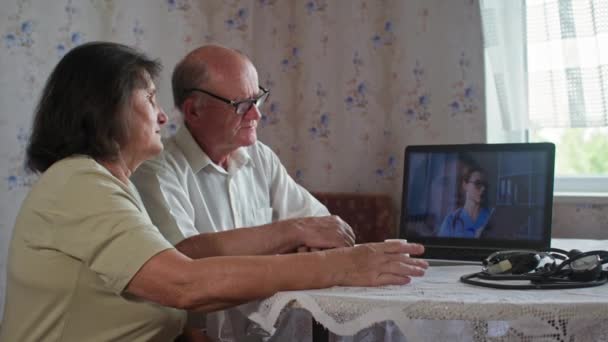 Сучасна медицина, літня пара пенсіонерів консультує про таблетки з лікарем через ноутбук, сидячи за столом в приміщенні — стокове відео