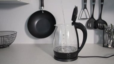 Ev halkı, mutfak gereçlerinin kaynama arkaplanı için şeffaf bir elektrikli su ısıtıcısına temiz soğuk su dökülür.