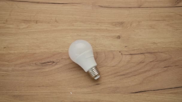 Электричество, белая лампа для освещения помещений лежит на деревянном фоне — стоковое видео
