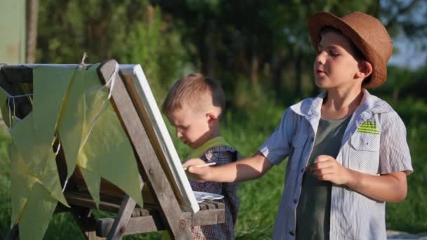 Sommarsemester, begåvade bröder måla bild med färger och penslar samtidigt koppla av utomhus på solig dag bakgrund av träd — Stockvideo