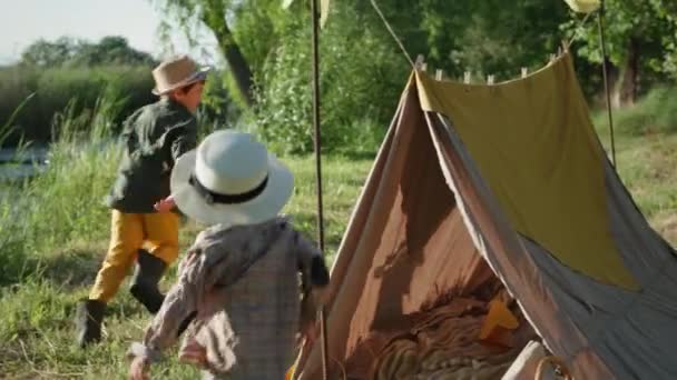 Aktív gyerekek, vidám kisfiúk szalmakalapban boldogan futkároznak a sátorban a nyári szünidőben a városon kívül — Stock videók