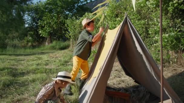 Kinderbeziehung, entzückender kleiner Junge hilft seinem älteren Bruder während eines Sommerurlaubs in einem Dorf ein Pergwam zu bauen — Stockvideo