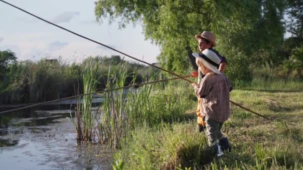 Kleiner Fischer, fröhliche männliche Kinder mit Strohhüten und Angelruten fischen in den Sommerferien in der Natur im Fluss — Stockvideo