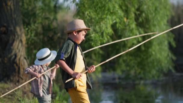 Rybaření, malý rybář s bratříčkem používají dřevěné pruty k rybaření v řece během letních prázdnin v obci — Stock video