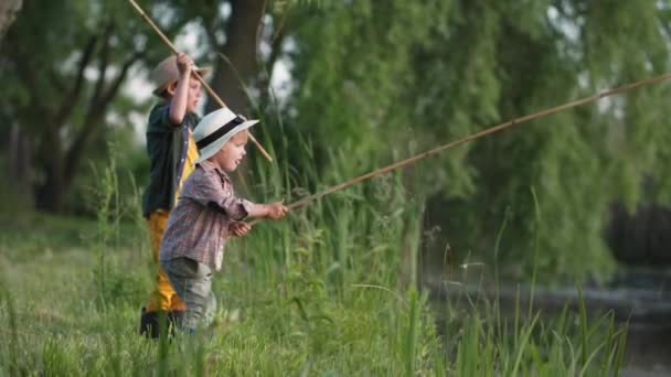 Outdoor-Spiele, lustige männliche Kinder in Strohhüten angeln begeistert mit Holzruten im Fluss während der Sommerferien außerhalb der Stadt im Dorf — Stockvideo