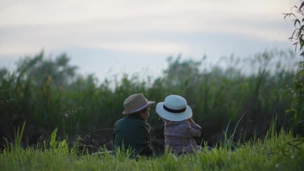 Pescador pequeño, hermanos alegres en sombreros de paja con cañas de pescar en sus manos coger peces en la orilla del río sentado en el prado entre cañas al atardecer — Vídeos de Stock