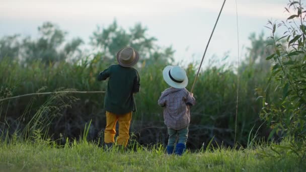 Outdoor recreation, cute little boys have fun near river and fish with a fishing rod background of reeds — Stock Video
