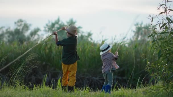 Vacaciones de verano, adorables niños pequeños con cañas de pescar en sus manos peces en el estanque mientras se relaja por el río en el césped verde en la noche cálida — Vídeos de Stock