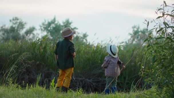 Happy childhood, adorable little boys in straw hats have fun fishing with fishing rods in river among trees and reeds — Stock Video