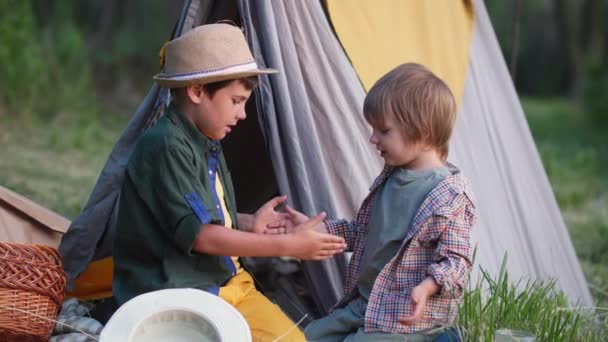 Helg i byn, bedårande söta bröder har kul att spela händerna medan du sitter i en wigwam samtidigt koppla av utomhus med träd — Stockvideo