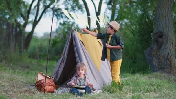 Utomhus barn, söta pojkar njuta av att tillbringa tid tillsammans och bygga tepees på gräsmattan bland träden samtidigt koppla av på landsbygden — Stockvideo