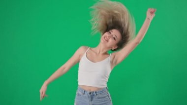 Uzun saçlı profesyonel bayan dansçı aktif olarak dans ediyor ve başını sallıyor, gülümsüyor ve yeşil ekrandaki kameraya bakıyor, kroma tuşlu.