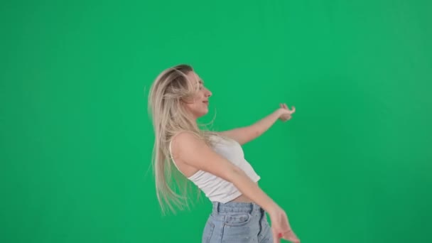 Professionele vrolijke vrouwelijke danser met lang haar draait en danst op een boze achtergrond, glimlacht en kijkt naar camera op groene achtergrond — Stockvideo