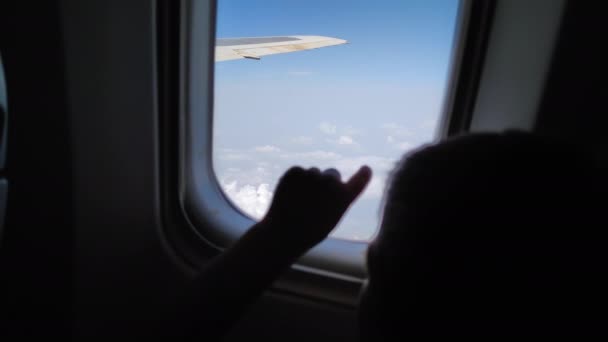 Child passenger in an airplane flies with beautiful view outside the window, curious little boy strokes his finger on the glass during the flight — Wideo stockowe