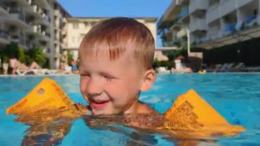 child learning to swim, water safety, little boy with yellow inflatable oversleeves swims in pool outdoors