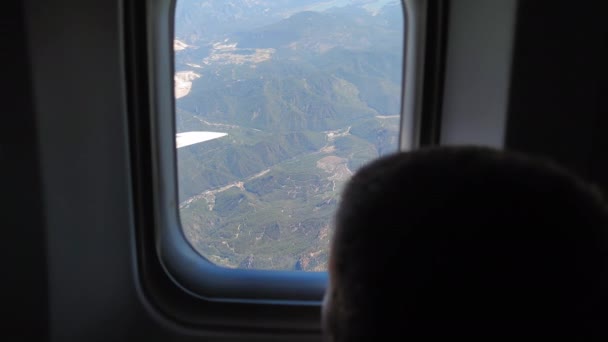 Curious little passenger looks out of the plane window at beautiful view of mountains, child boy during an airplane flight — Wideo stockowe