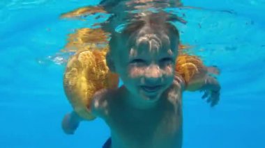 water safety, kid learning to swim under water with open eyes, little boy with yellow inflatable oversleeves swims in the pool