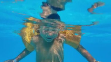 child learns to swim under the water, happy little boy with yellow inflatable oversleeves swims in outdoor pool