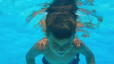 little boy learns to swim under water with open eyes, child swims in the outdoor blue pool during active summer vacation