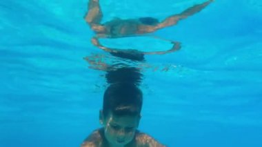 child dives under water with open eyes, little boy swims in the blue water of pool during summer vacation