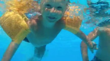 children dives under water with open eyes, little boys swims in the blue water of pool during summer vacation