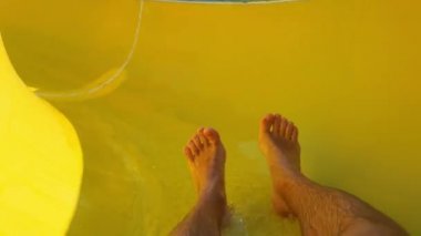 enjoying on waterslide during summer vacation, feet of man slides down the pool in water park on holiday resort