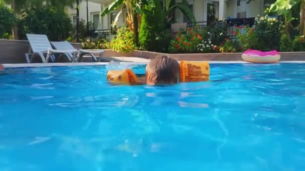 Criança aprende a nadar debaixo d 'água durante as férias de verão, menino pequeno com oversleeves infláveis amarelos na piscina — Vídeo de Stock