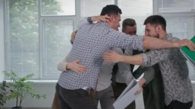Başarılı iş, mutlu erkek çalışma takımı iyi haberlere sevinir ve ofis toplantısı sırasında birbirlerine sarılırlar.