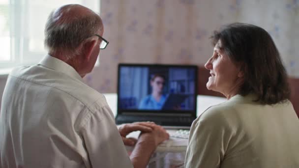 Eşlerin omuzlarının üstündeki bilgisayar ekranı, dizüstü bilgisayar kullanan yaşlı hastalar doktorla evdeki haplar hakkında konuşuyorlar — Stok video