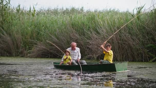 Familia descansar juntos fuera, abuelo y nietos pesca con palos en barco en el lago en el fondo de cañas verdes — Vídeos de Stock