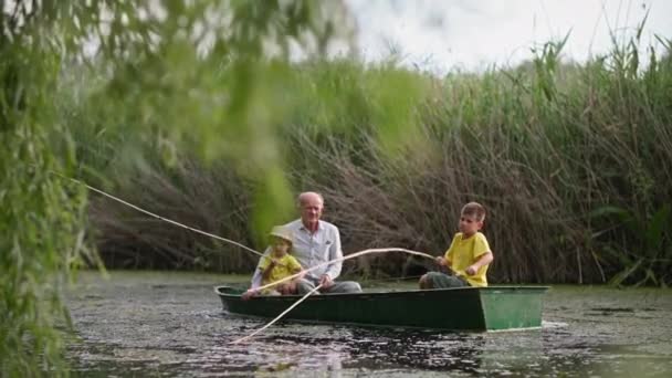 Granddad and grandsons on boat catch fish from river on background of green reeds, family rest together outdoors — Stock Video