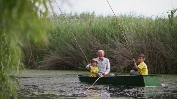 자연 속에서 휴식을 취하는 아이들, 할아버지와 손자들은 함께 강에서 낚시를 하고 있습니다. 푸른 갈대와 물의 경치를 배경으로 말이죠. — 비디오