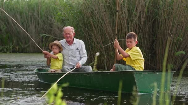 Loving grandfather teaches his grandchildren to fish, family in boat near the reeds has fun together on summer holidays in the village — Stock Video