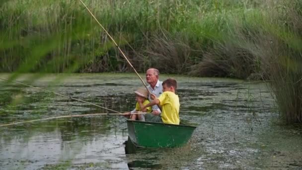 Abuelo enseña a los nietos a pescar, familia con cañas de pescar en barco en el río cerca de las cañas — Vídeo de stock