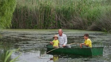 Balıkçı torunlarına gölde balık tutmayı öğretiyor. Sazlıkların arka planında olta kamışlarıyla.
