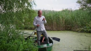 Gölde tatiller, bir teknede duran büyükbaba küçük torunuyla yeşil çamurlu nehir boyunca kürek çekiyor.