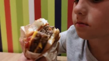 Aç küçük çocuk iştahlı hamburger yer. Çocuk kafesinde çocuk için zararlı bir yemek.