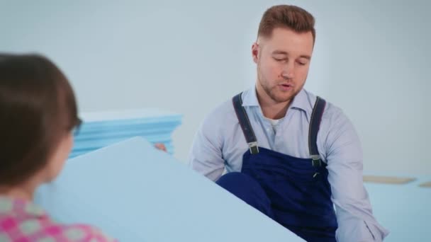 Man met werkkleding bespreekt met jonge vrouw piepschuim voor isolerende vloer voor het leggen van laminaat in appartement — Stockvideo