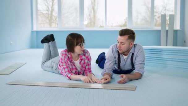 Женщина и мужчина лежат на изолированном полу перед укладкой ламината, радуясь работе в помещении — стоковое видео