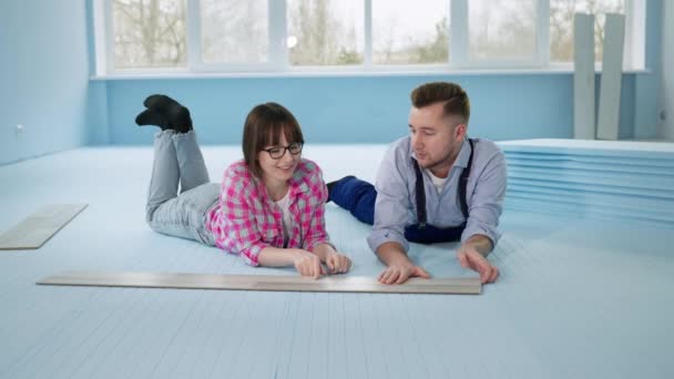 Par som ligger på golvet med isolerat polystyrenskum innan de lägger laminat i lägenheten under renoveringen — Stockvideo