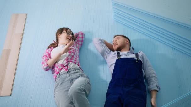 Spouses are resting after work lie on expanded polystyrene foam while insulating floor before laying laminate in apartment during renovation and finishing work, top view — Stock Video