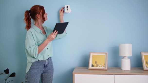 Seguridad del hogar inteligente, chica con PC tableta ajusta la cámara mientras está de pie cerca de la pared, la instalación y comprobación de videovigilancia en el interior — Vídeos de Stock